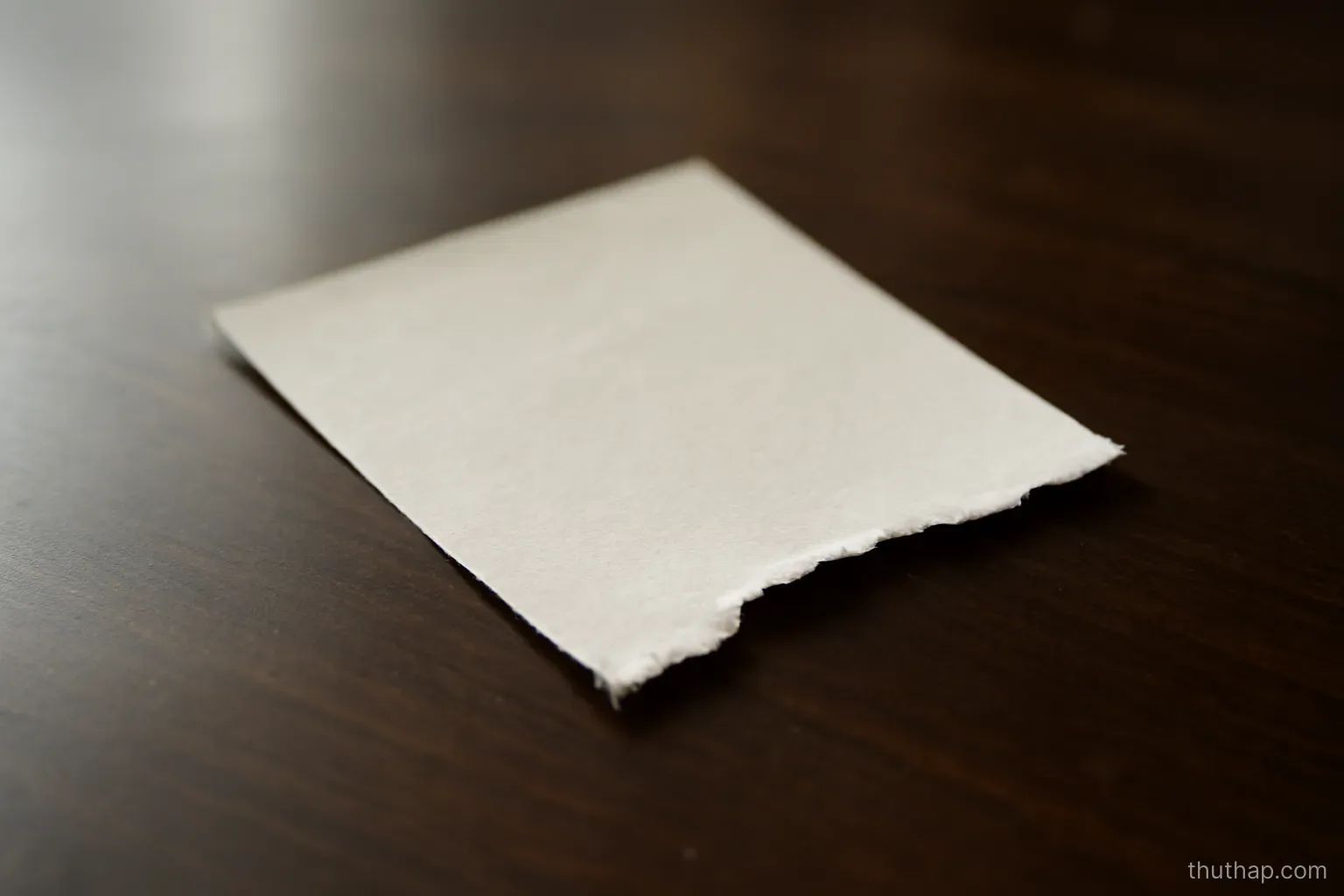 a torn corner of thick paper resting alone on a dark polished table surface